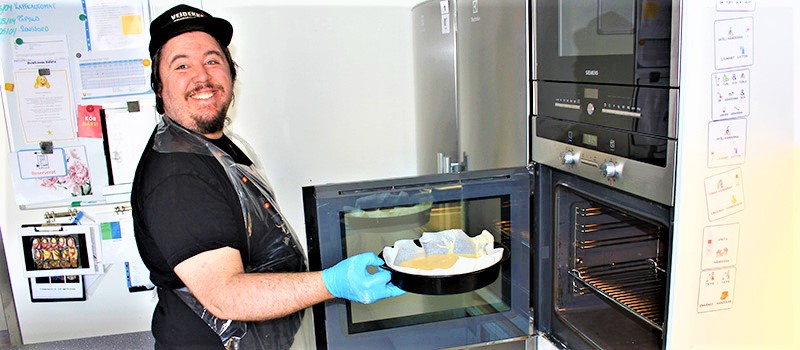 Arbetstagare ställer in en ugnsform fylld med smet i ugnen för att göra en citronkladdkaka på Café Håbo.