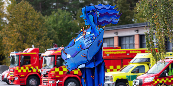 Den blå statyn Brinnande väktare med brandbilar i bakgrunden