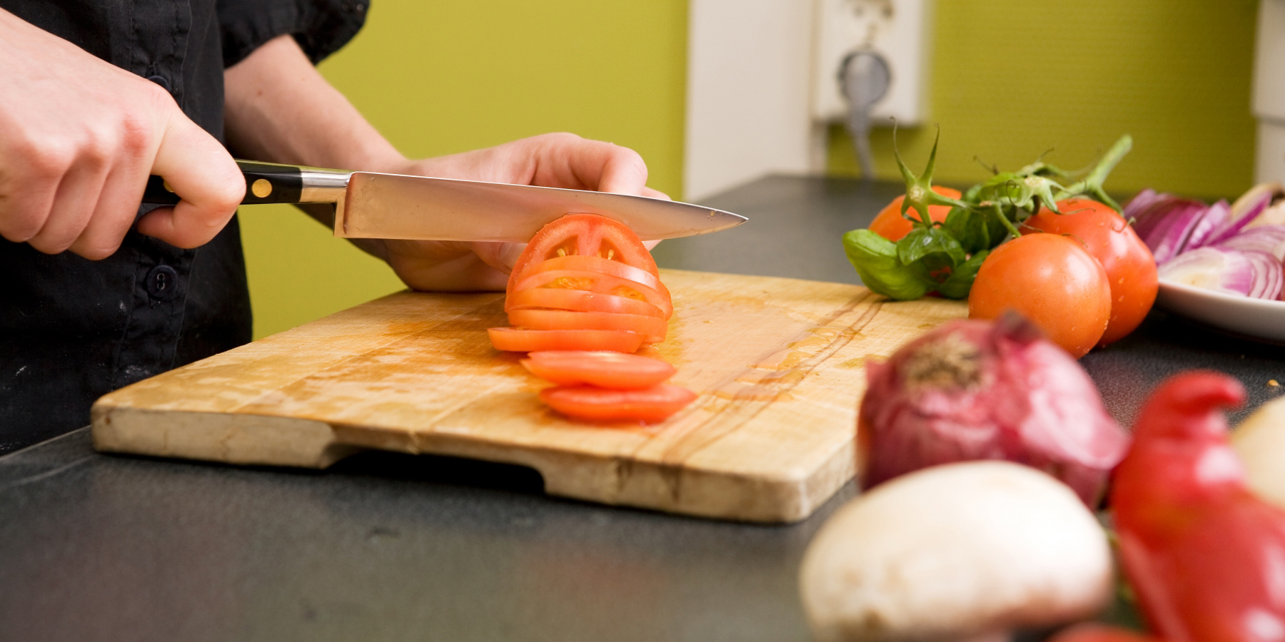 En kock i svart skjorta skär tomater och lök på en skärbräda.