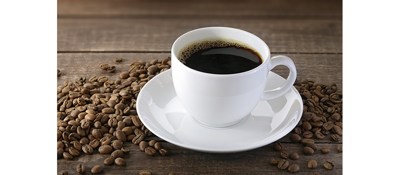 En kopp med kaffe, runtom ligger det kaffebönor 