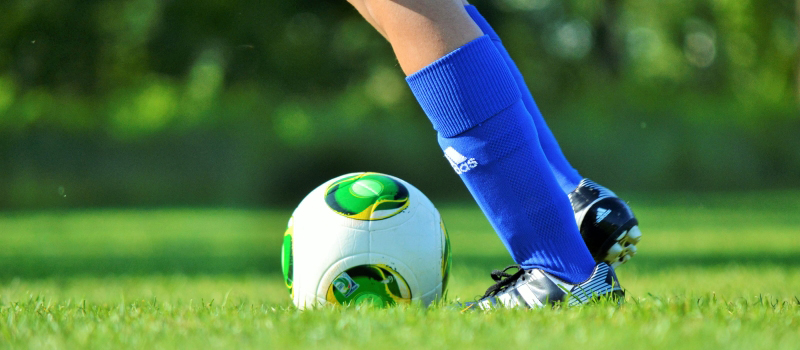 Fötter och en fotboll på en fotbollsplan