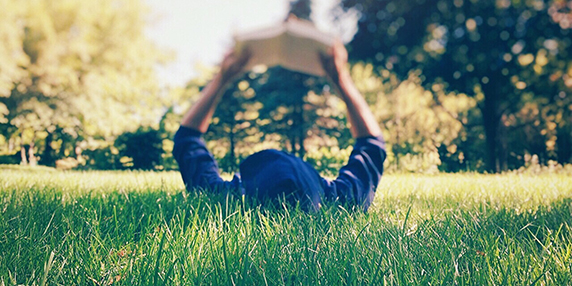 Person som ligger i gräset i solen och läser