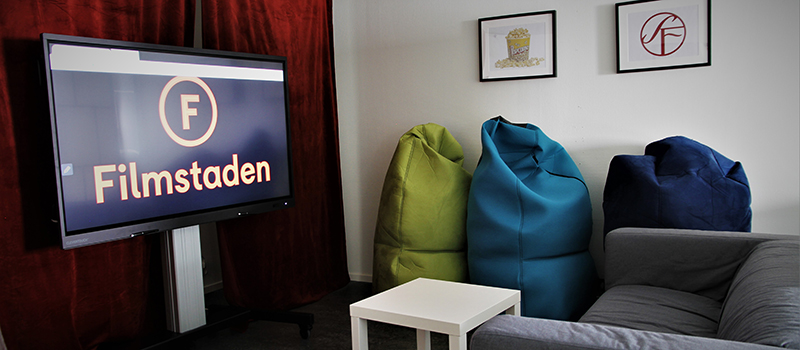 Bild på multimediarummet, stor 60-tums touchskärm framför soffa och sittkuddar.