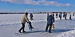 Två personer med sparkar på en is och barn i bakgrunden.